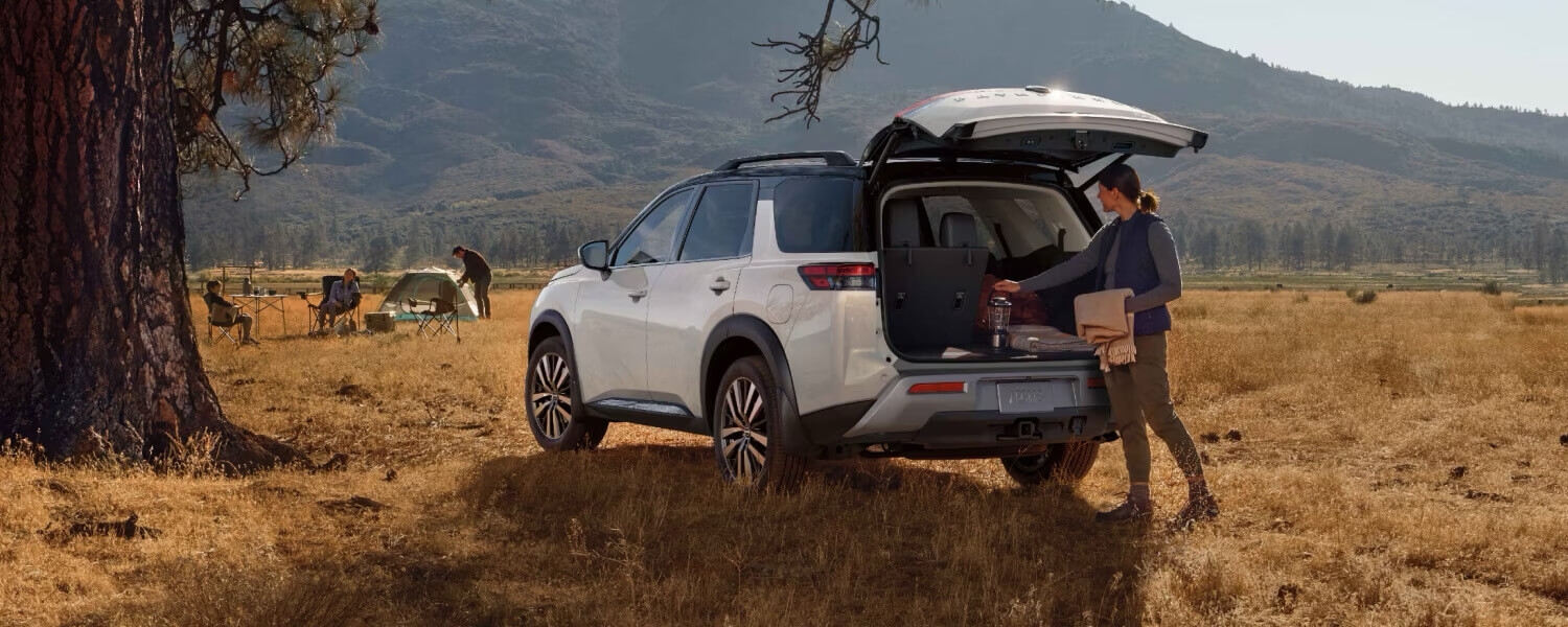Femme chargeant le coffre du Nissan Pathfinder 2025 garé en nature.
